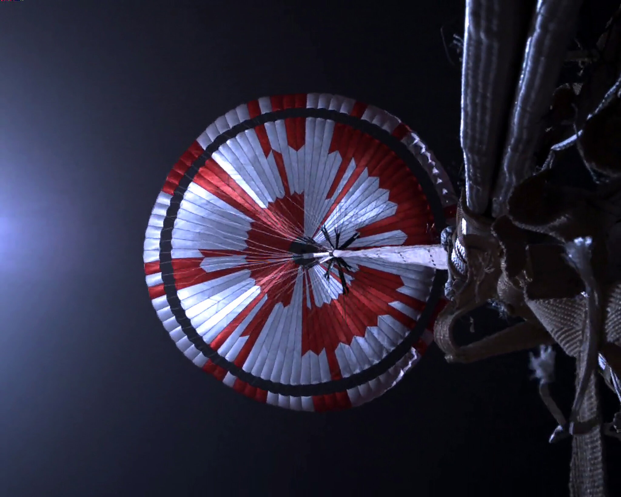 Parachute of the Perseverance rover during landing, with the code "Dare Mighty Things" embedded in the pattern.