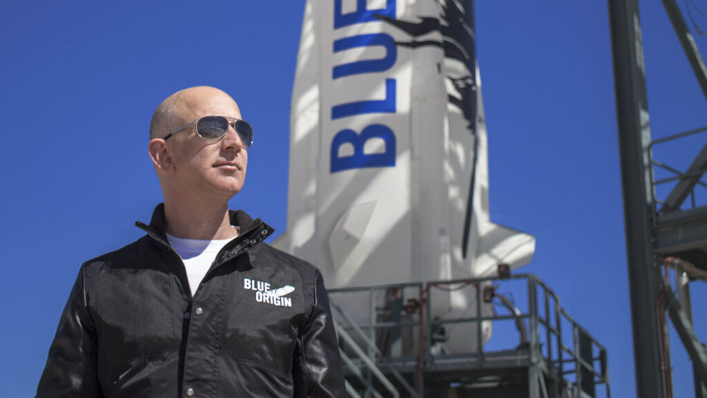 Jeff Bezos in sunglasses standing in front of Blue Origin's New Shepard rocket