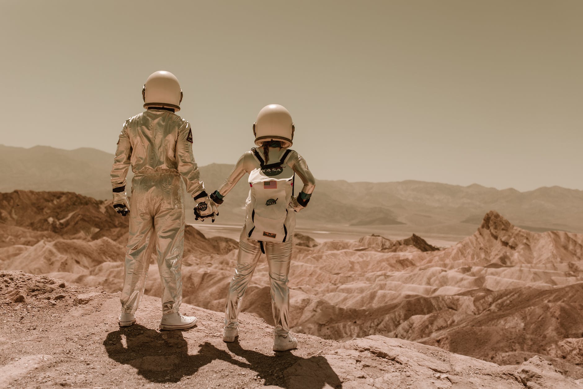 astronauts holding hands standing on brown mountains